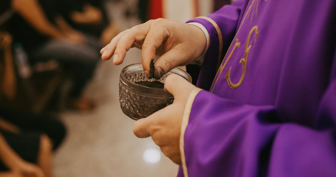 Primo piano delle mani di un sacerdote che prende della cenere da una ciotola
